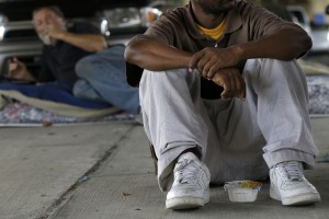 Erick Richardson, who is homeless and is among about 150 people living under the Pontchartrain Expressway overpass, sits with a container of cereal in New Orleans, Wednesday, Aug. 13, 2014. (AP Photo/Gerald Herbert)