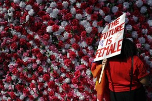 Angela Henderson, front, shows her photos to Joseph Banco as they stand in front of a wall decorated with artificial flowers during the Day Without a Woman protest Wednesday, March 8, 2017, in Los Angeles. Many American women stayed home from work, joined rallies or wore red Wednesday to demonstrate how vital they are to the U.S. economy, as International Women's Day was observed with a multitude of events around the world. (AP Photo/Jae C. Hong)