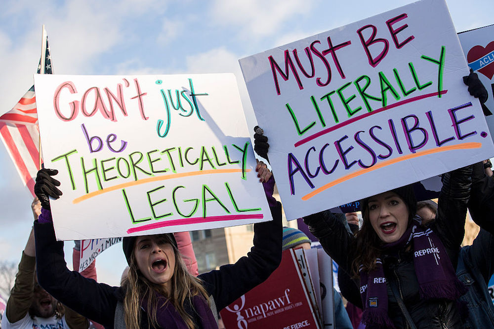 protesters holding signs reading 'can't just be theoretically legal' 'must be literally accessible'