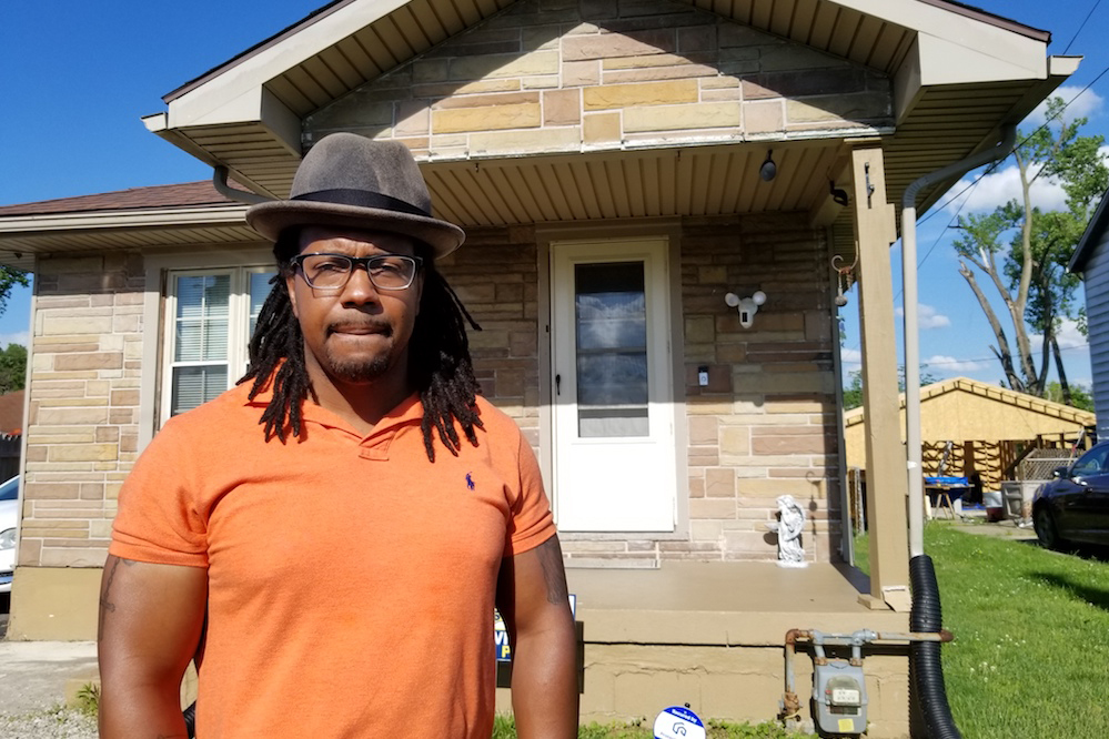 A man in a hat standing in front of a front porch.