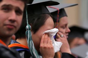 college students in graduation gowns. one cries into a tissue.